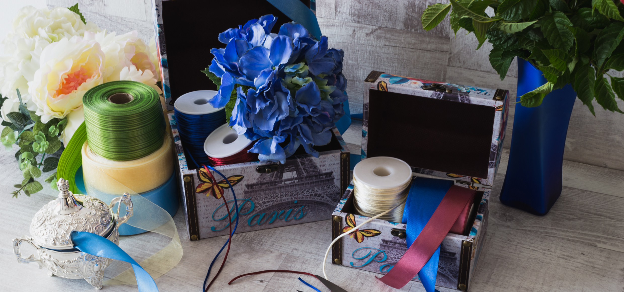 scena dintr-un atelier de arnjamente florale infatisand flori artificiale, doua cutii decorative, snururi si panglici colorate